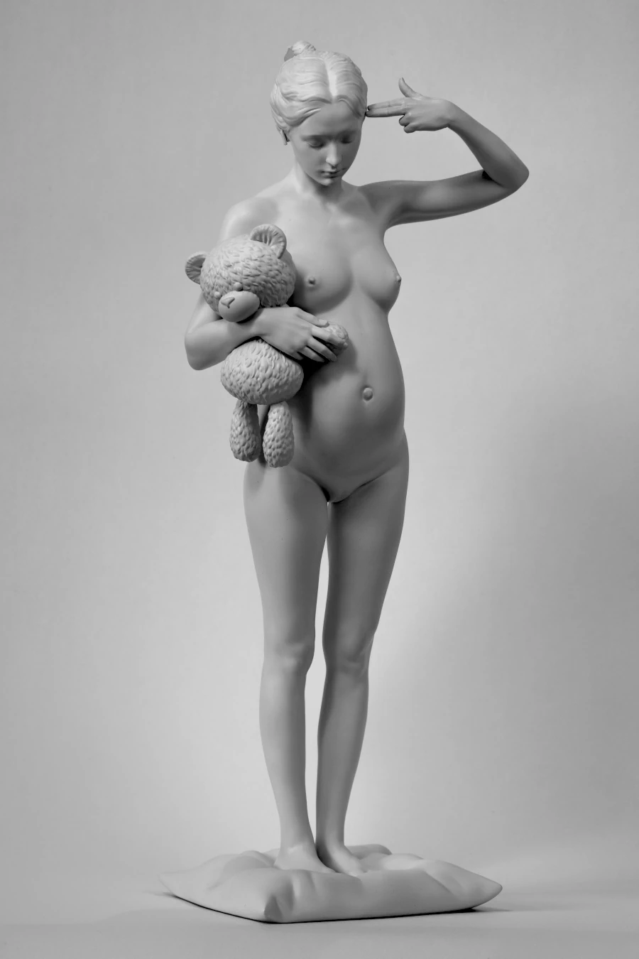 Piety, 2024. Monochrome sculpture of a pregnant woman holding a teddy bear with one hand raised to her head.
